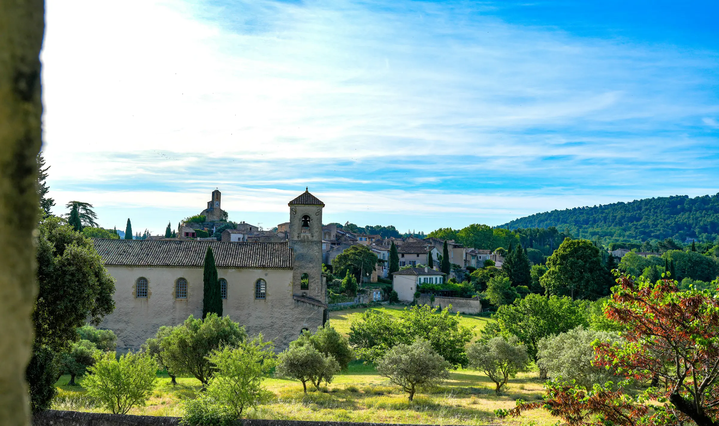 Un village provençal à flanc de colline, son clocher et son église de pierre au-dessus d'une oliveraie, un matin d'été